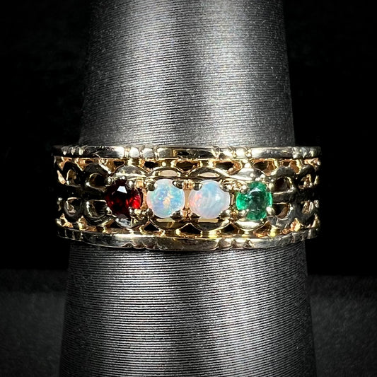 A gold woven-style mother's ring set with two opals, an emerald, and a garnet shown from the front.