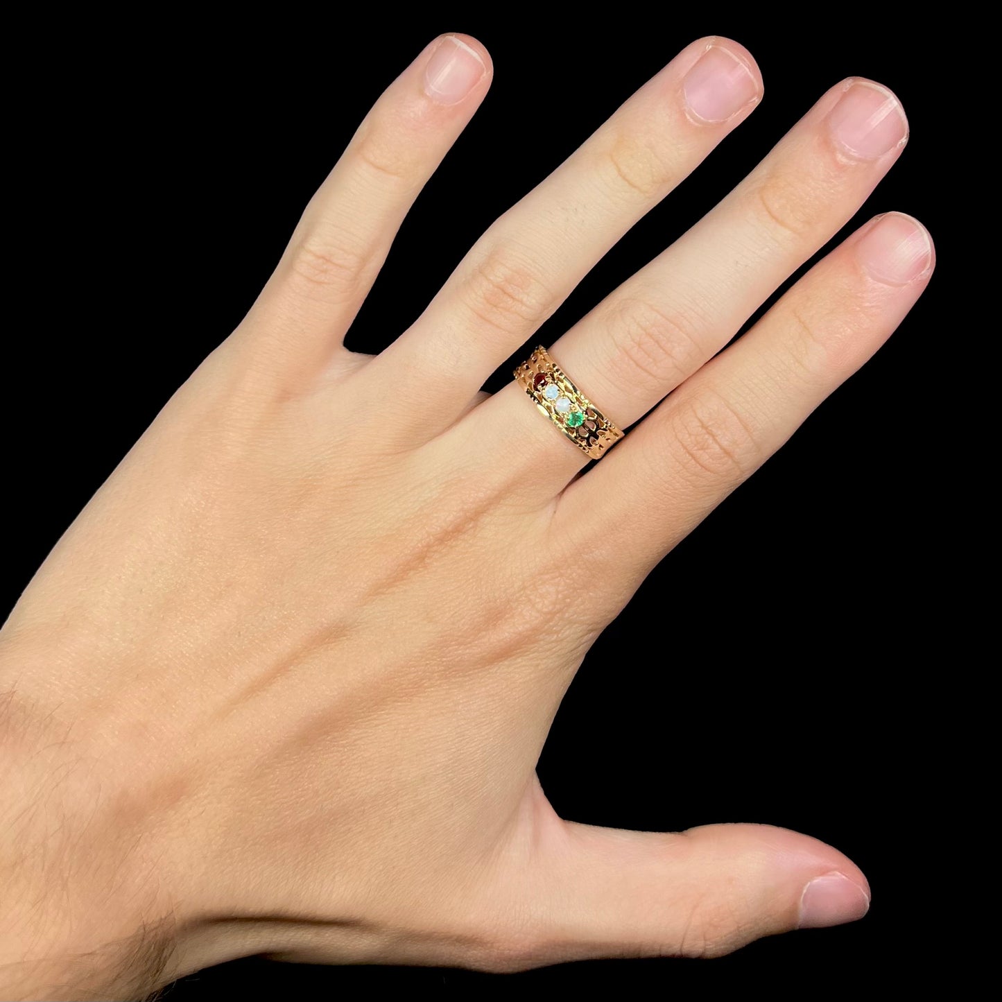 A gold woven-style mother's ring set with two opals, an emerald, and a garnet worn on a hand.