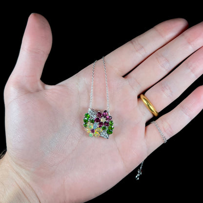 An opal, garnet, and chrome diopside flower necklace held in a hand against a black background.