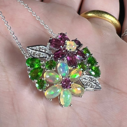 A sterling silver opal and garnet flower necklace shown close-up in the palm of a hand at an angle.