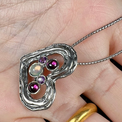 A sterling silver heart necklace set with a round Ethiopoian opal, two amethysts, and two rhodolite garnets.