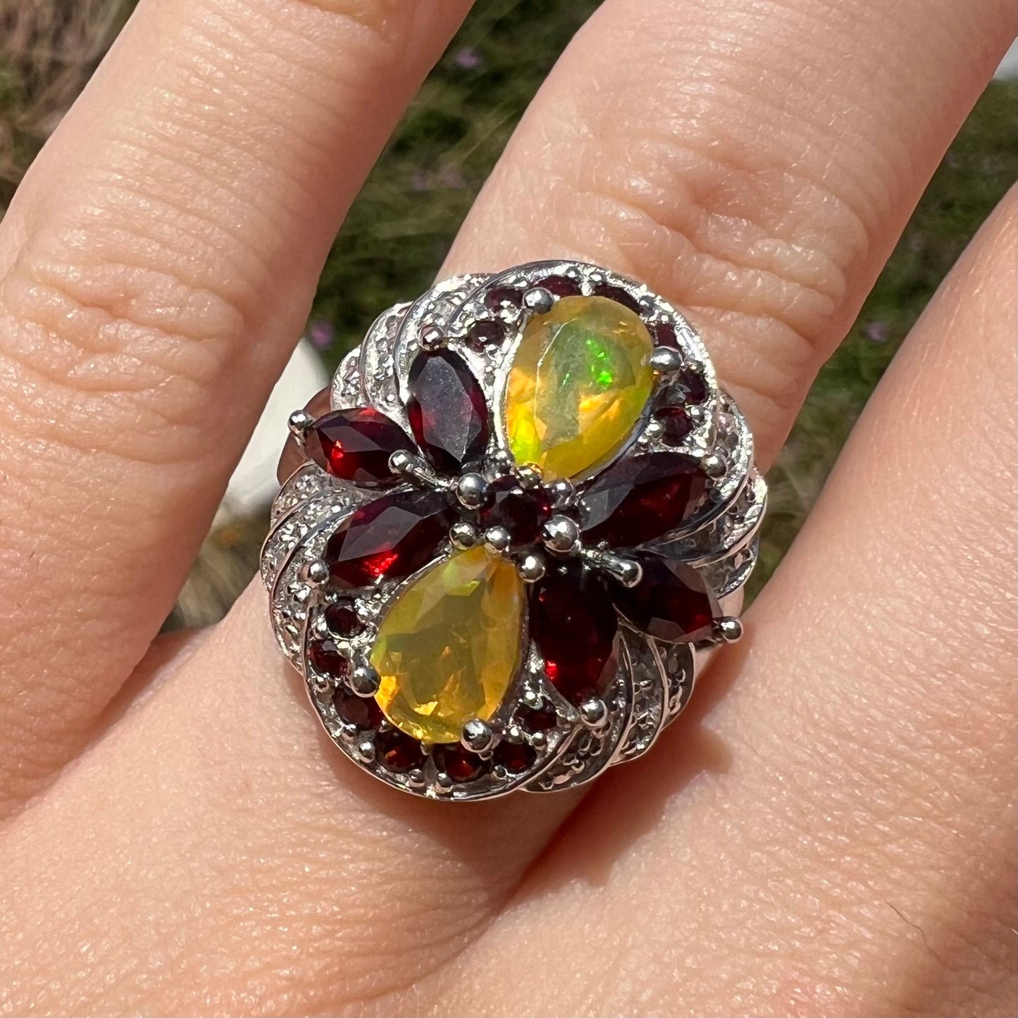 Sunlit close-up of a sterling silver Ethiopian opal and garnet infinity-design ring with diamond accents.