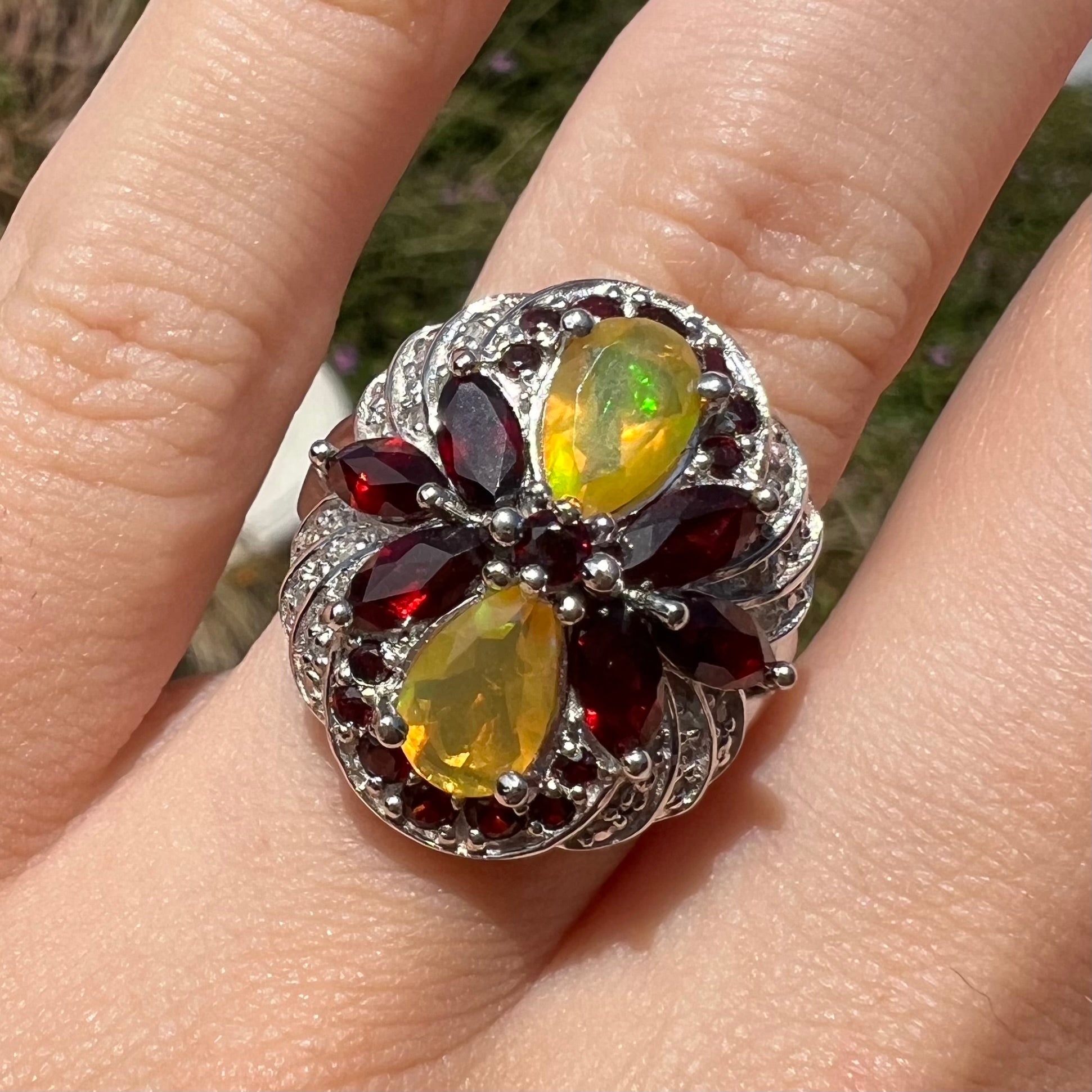 Sunlit close-up of a sterling silver Ethiopian opal and garnet infinity-design ring with diamond accents.