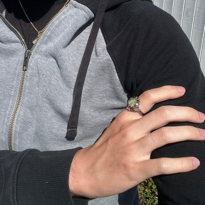 An opal and multi-color gemstone ring worn on a hand that's resting on the model's shoulder.