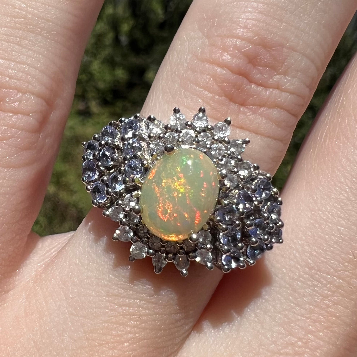 Close-up sunlit view of Ethiopian opal ring with spray of tanzanites and white topaz, worn on finger