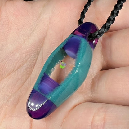 Angled close-up of an opal in glass necklace by Utah artist, Nathan Snyder, held in a hand.