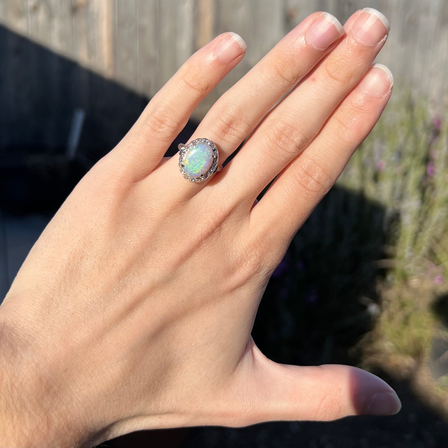 A vintage opal and diamond halo enggagement ring on a hand in the sunlight.