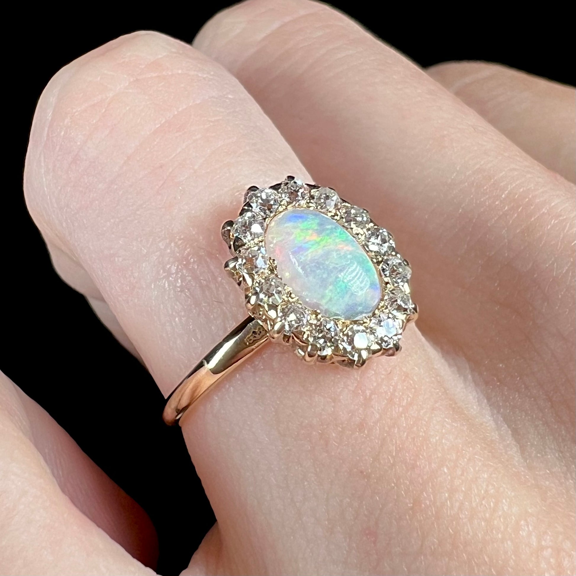 A yellow gold opal and diamond halo engagement ring on a hand.  The diamonds are Old European Cut.