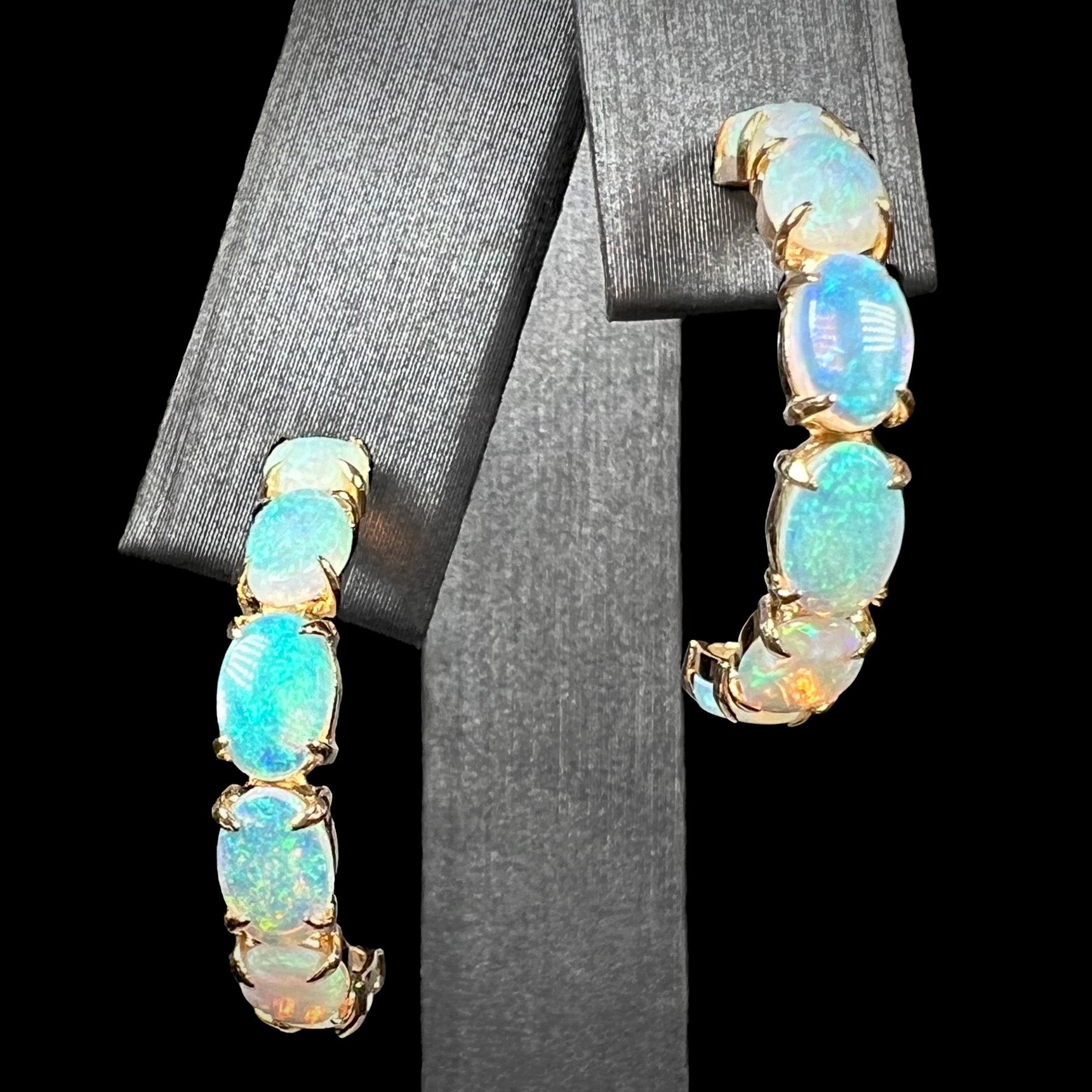 A pair of crystal opal hoop earrings in 14k gold on a black background, front macro view.