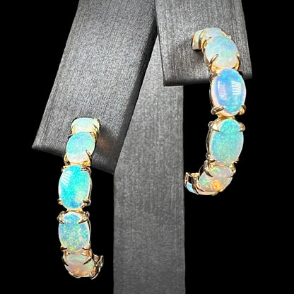 A pair of crystal opal hoop earrings in 14k gold on a black background, front macro view.