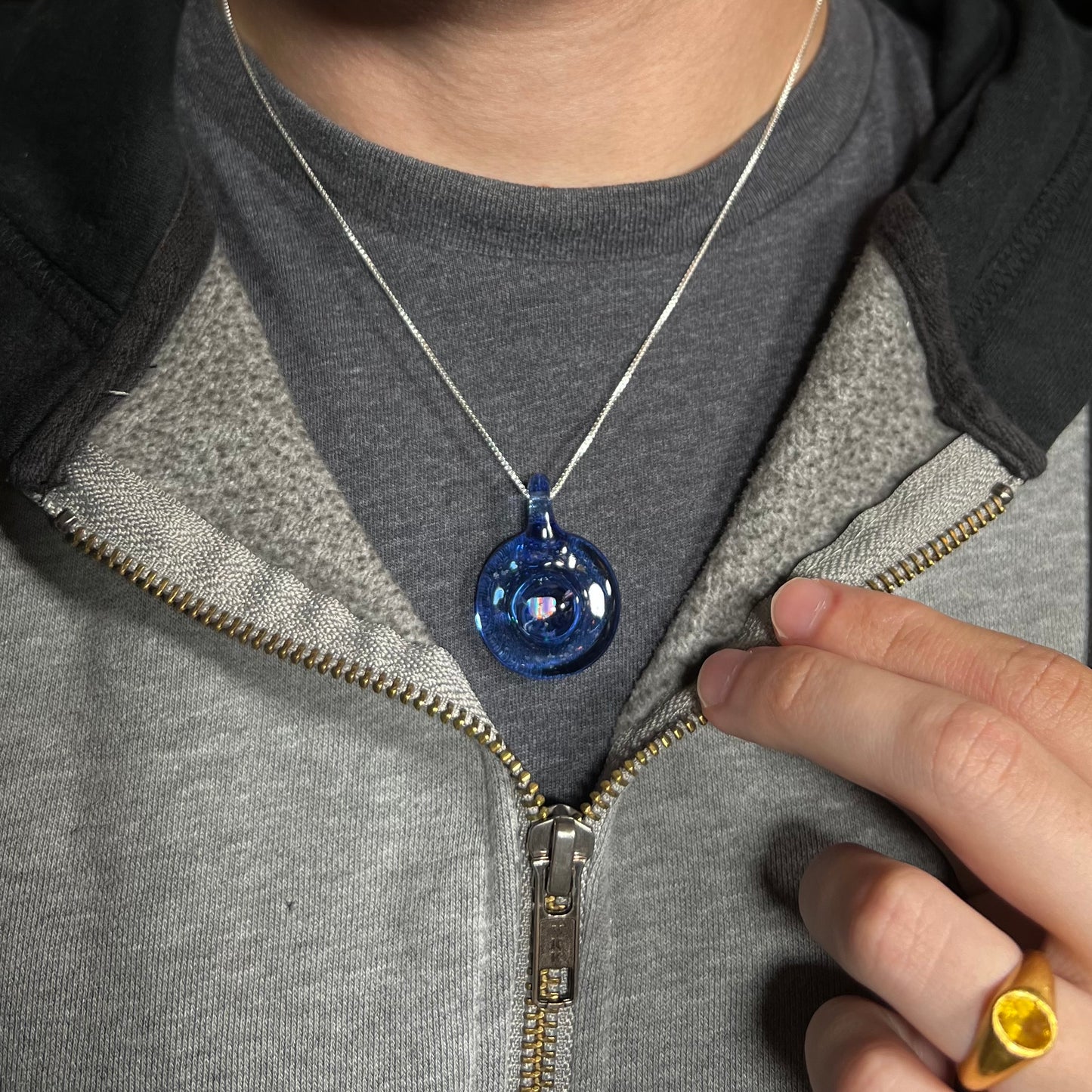 An opal in round, blue glass necklace, worn around a neck against a dark shirt.