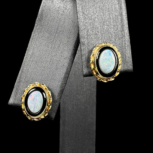 Macro close-up of a pair of gold stud earrings set with opals in onyx shown from front on earring display against black background.
