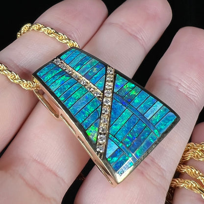 Angled close-up of an opal inlay and diamond slider pendant shown held in a hand under LED studio lighting.