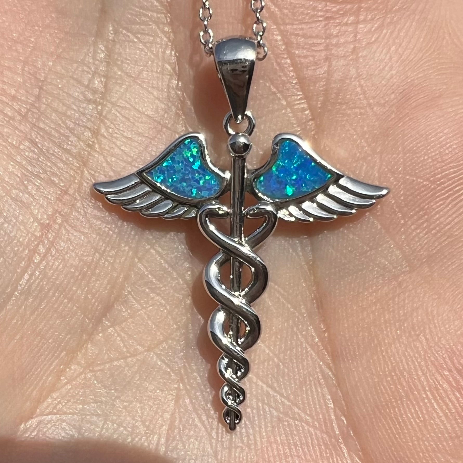 A silver plated medical caduceus pendant with blue lab-created opal inlay.