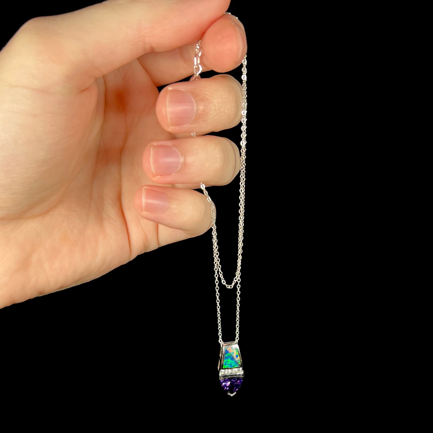 Hand dangling a sterling silver opal inlay and purple CZ drop necklace from its silver cable chain.