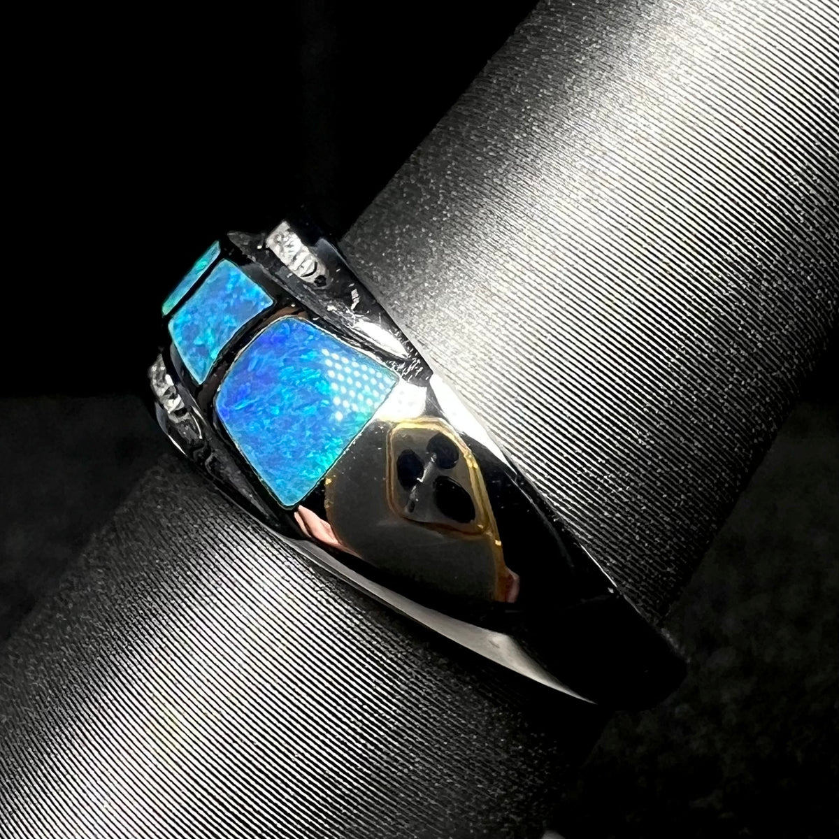 Side view of a blue opal inlay ring with diamond accents in 14k white gold, shown on ring display, the ring's polished shank in focus