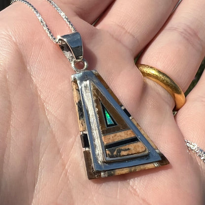 A sterling silver Australian opal, picture jasper, and onyx inlay pendant shown close-up at an angle in sunlight.