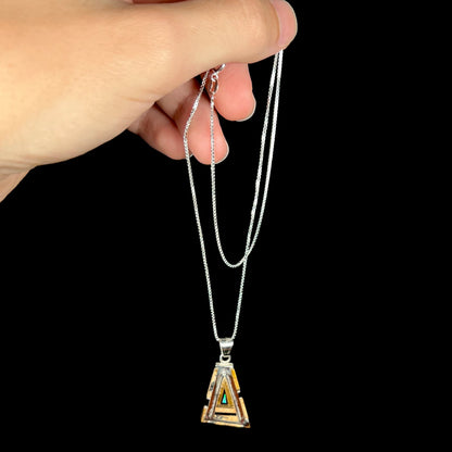 A sterling silver Australian opal, picture jasper, and onyx inlay necklace, dangled from its chain by a hand.