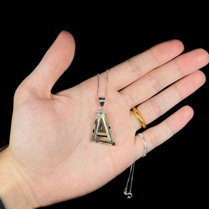 A sterling silver Australian opal, picture jasper, and onyx inlay pendant shown in a hand against a black background.