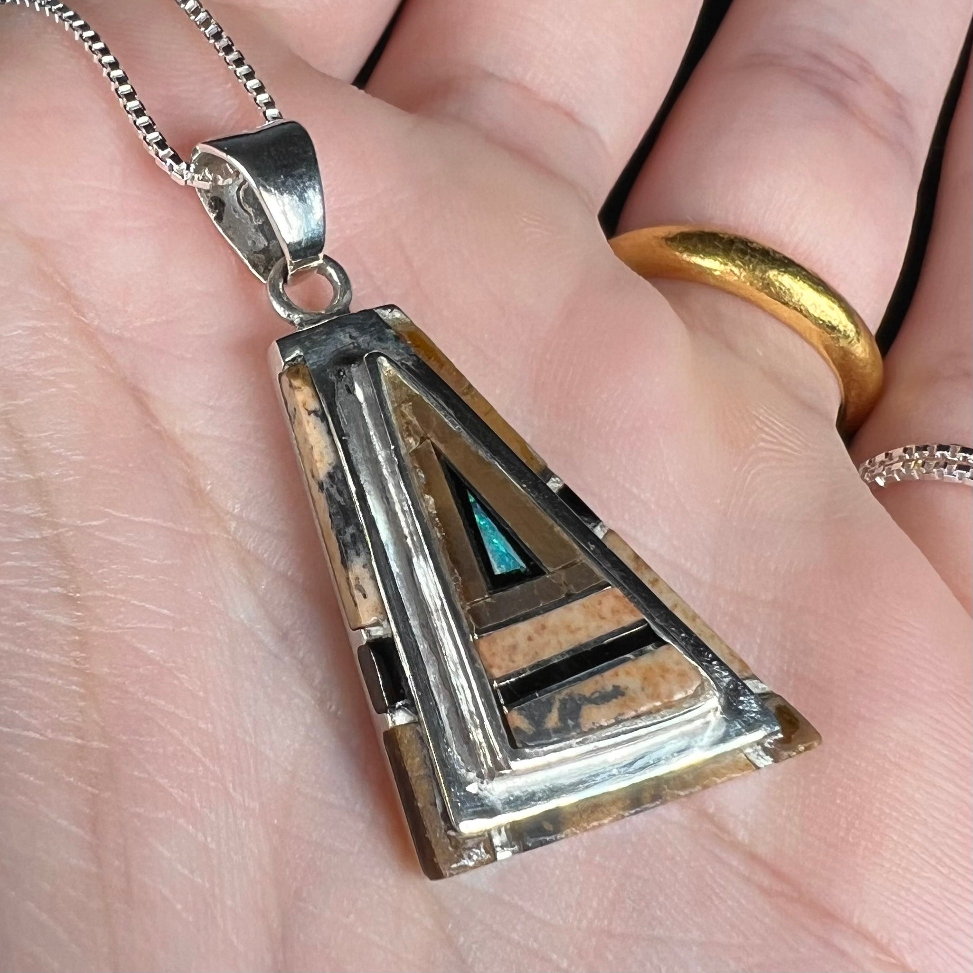 A sterling silver Australian opal, picture jasper, and onyx inlay pendant shown close-up from an angle in a hand.