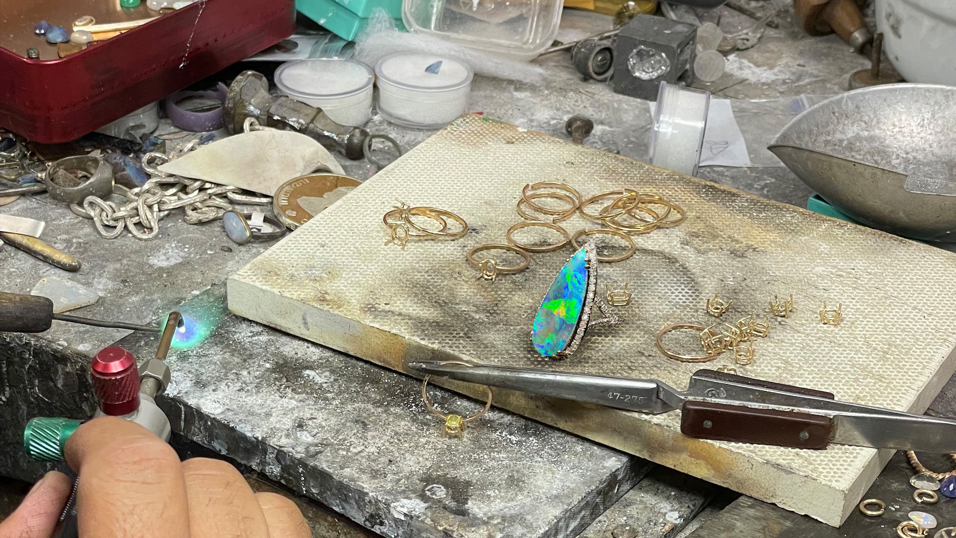 The crowded workbench of an Anaheim, California jeweler, strewn with gold rings an a pear shaped Australian boulder opal and diamond halo ring.