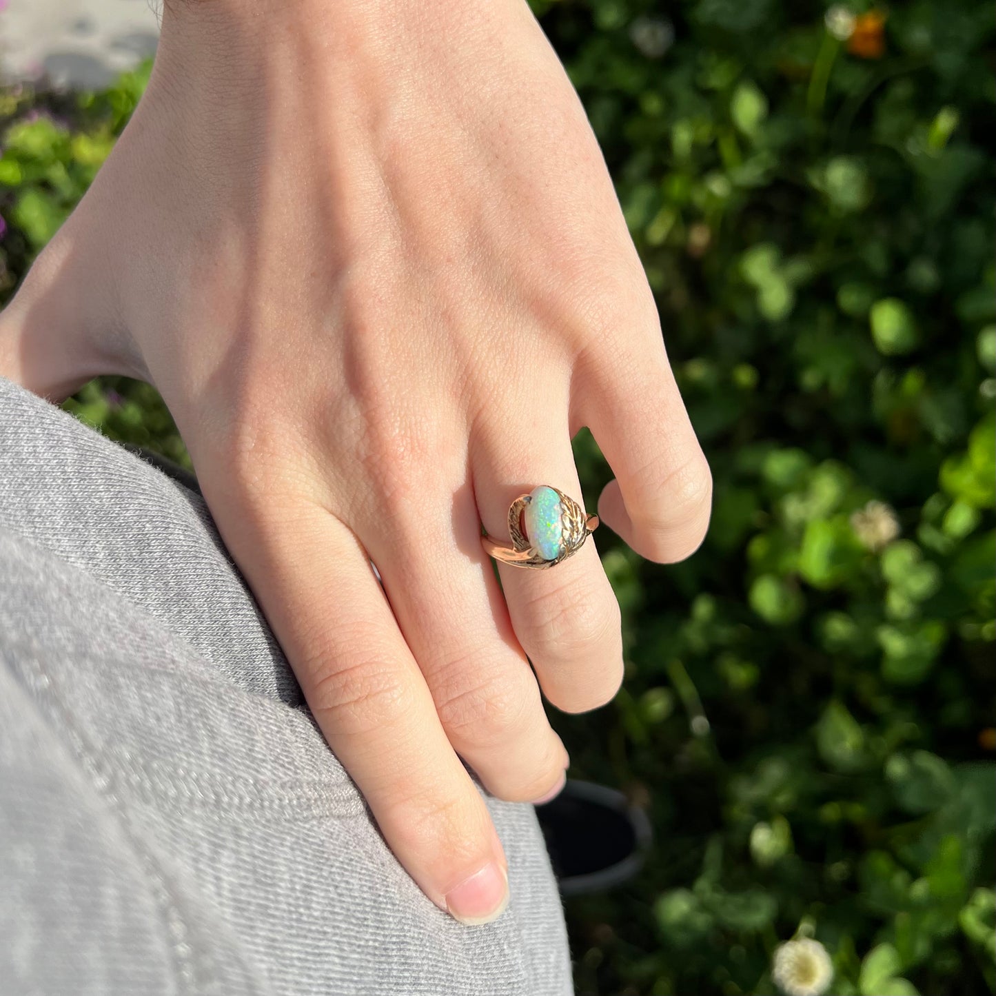 A yellow gold opal leaf ring worn on a finger.