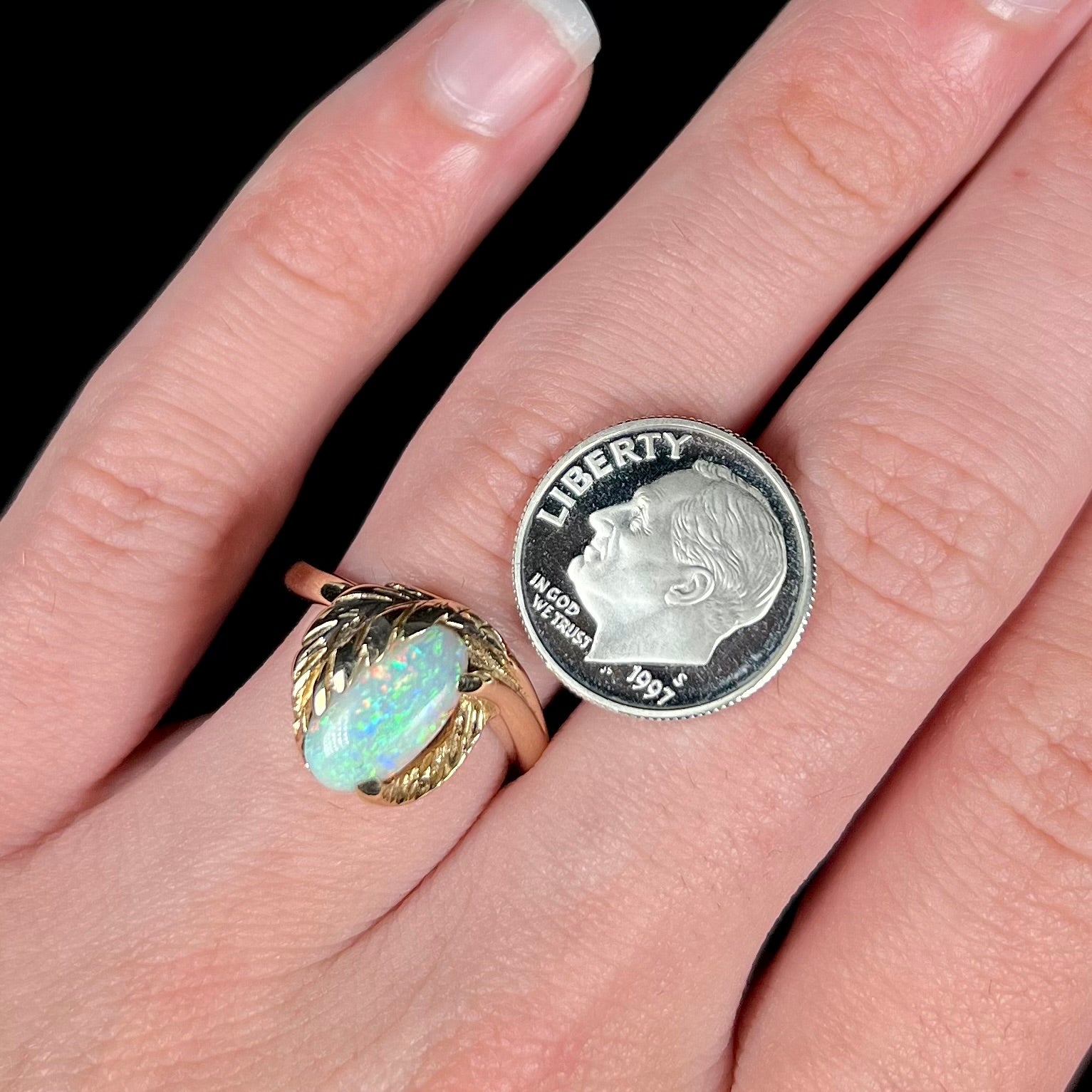 A yellow gold leaf-design opal ring next to a US dime coin for scale.