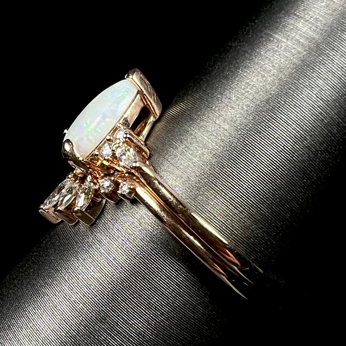 Side view focusing on shank of 14k rose gold opal and moissanite engagement ring set on ring display