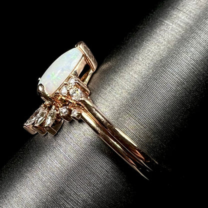 Side view focusing on shank of 14k rose gold opal and moissanite engagement ring set on ring display