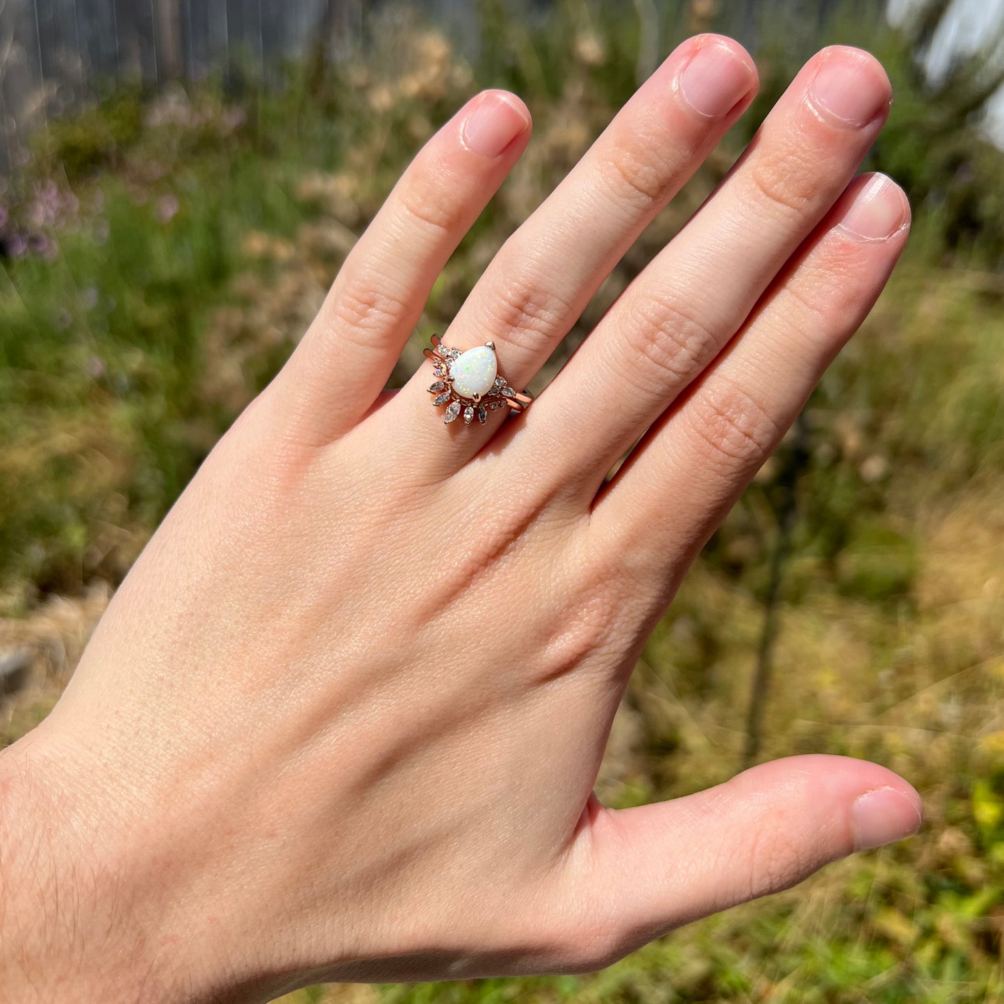 Hand wearing rose gold opal and moissanite engagement ring set in natural sunlight