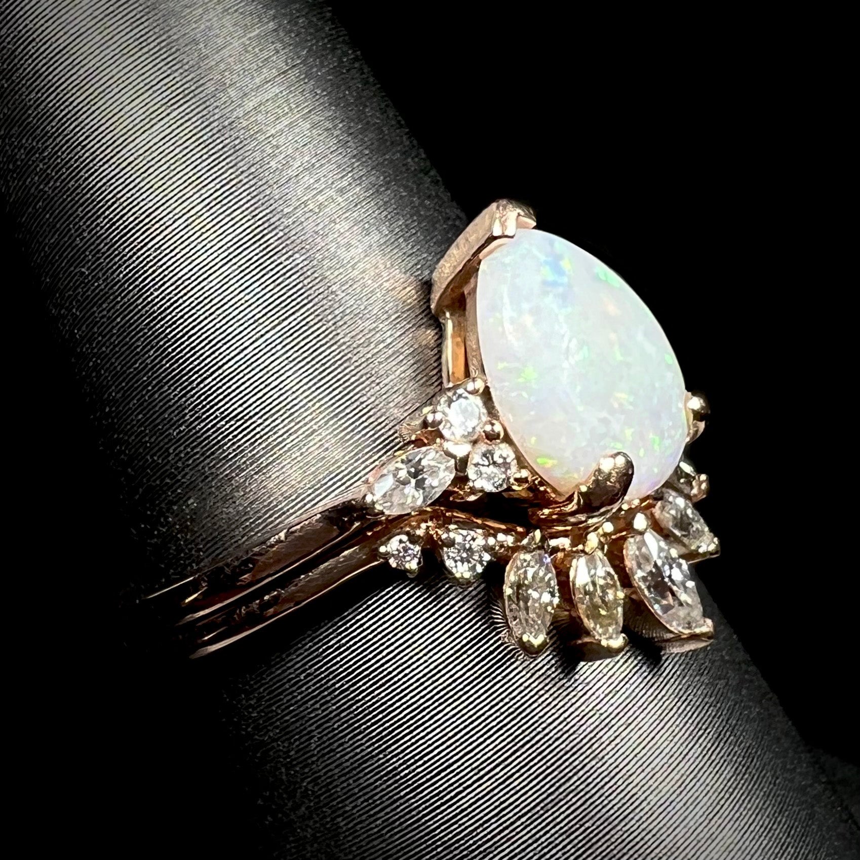 Teardrop shaped opal and moissanite wedding ring set in 14k rose gold, shown on ring display