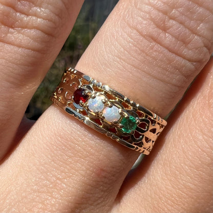 Close-up of a gold woven-style mother's ring set with two opals, an emerald, and a garnet in sunlight.