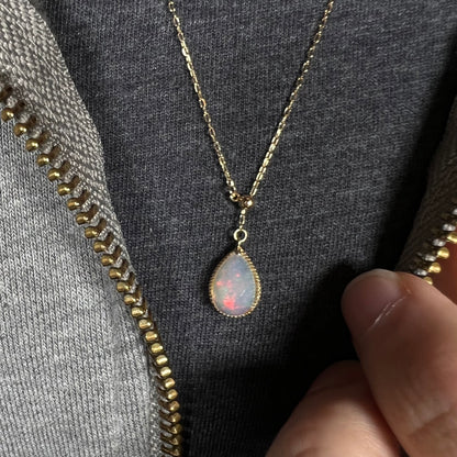 Close-up of the opal necklace worn at its longest setting over a black T-shirt. Red flashes are visible in the opal.