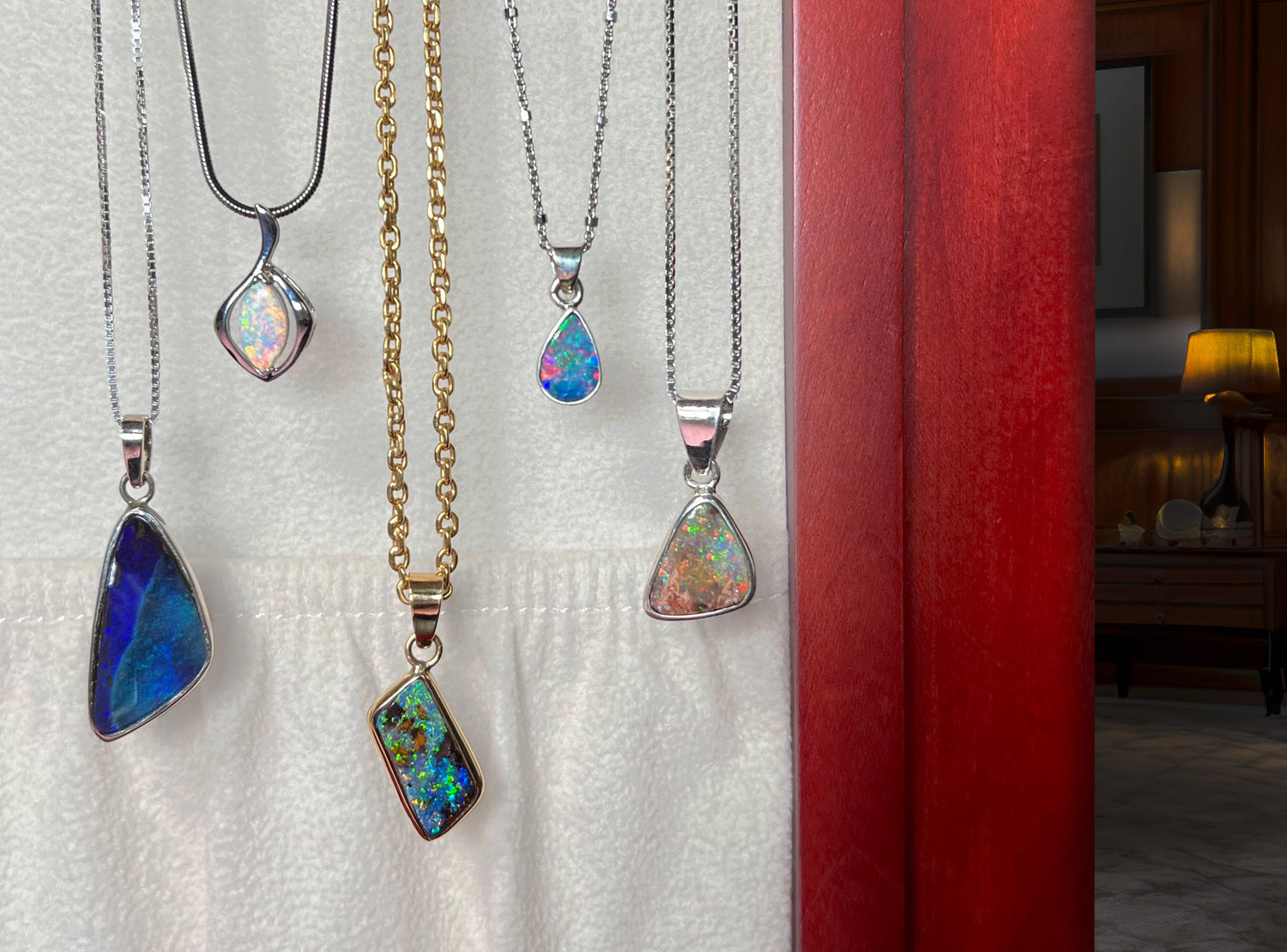 Five natural opal necklaces hang on gold and silver chains against a white felt backdrop.