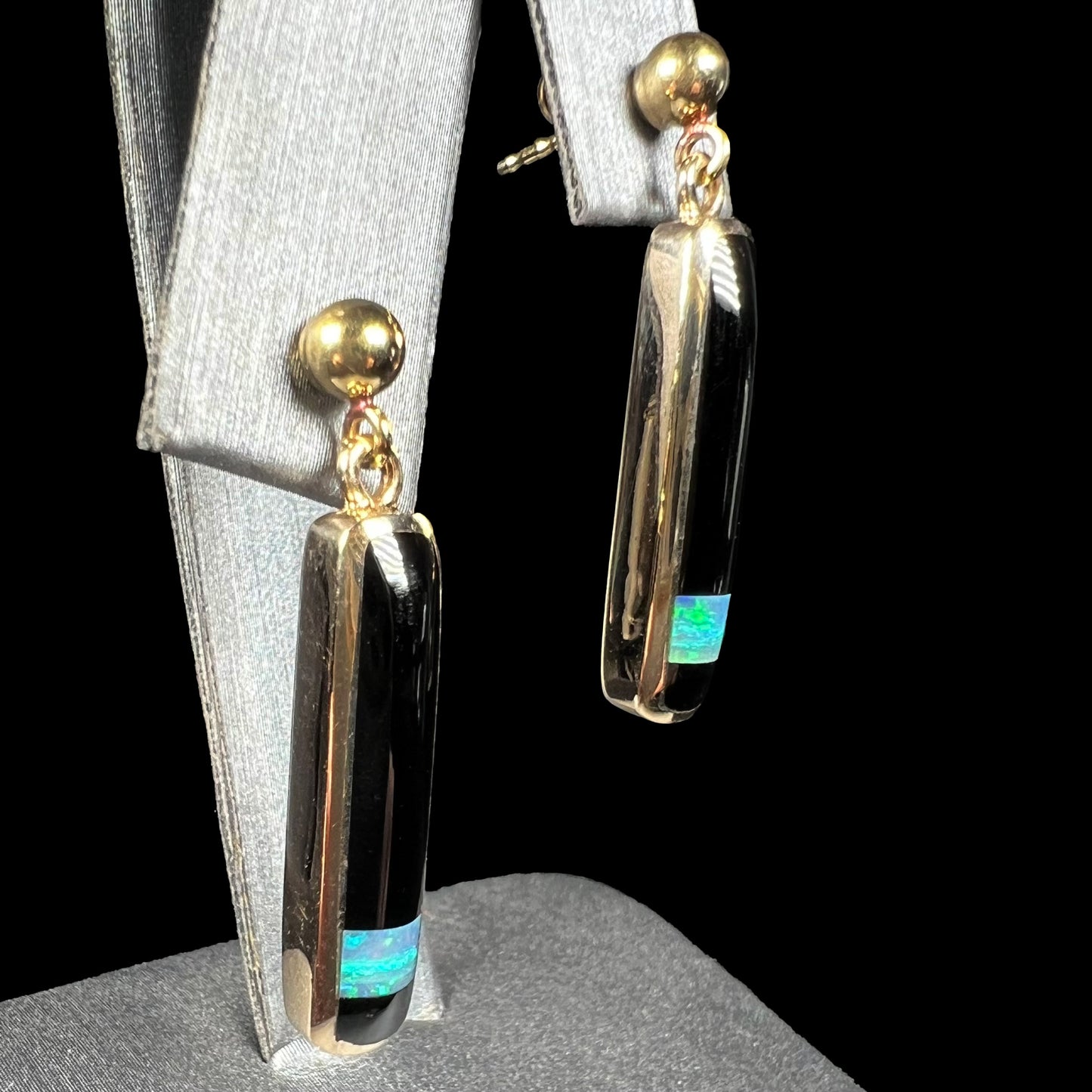 A pair of opal and onyx inlay dangle earrings, made from yellow gold, shown at an angle.