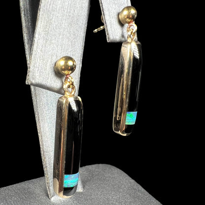 A pair of opal and onyx inlay dangle earrings, made from yellow gold, shown at an angle.