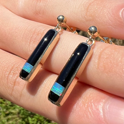 A pair of yellow gold opal and onyx inlay earrings shown close-up at an angle in the sunlight.