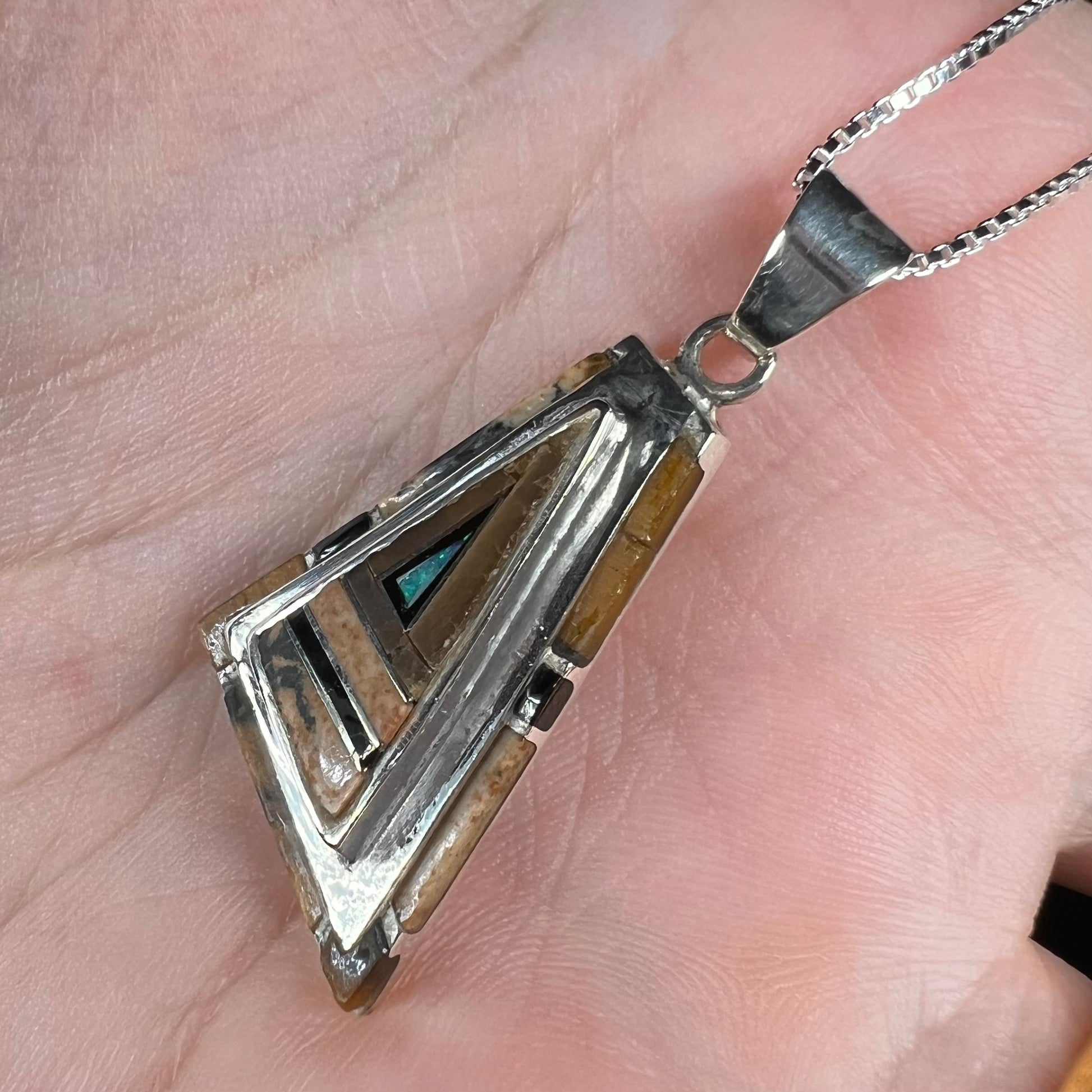 A sterling silver Australian opal, picture jasper, and onyx inlay pendant shown from an angle close-up in a hand.