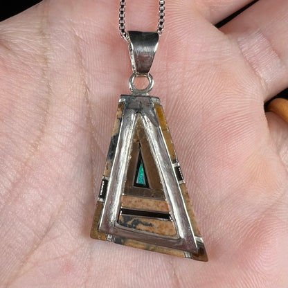 A sterling silver Australian opal, picture jasper, and onyx inlay pendant shown close-up in a hand.
