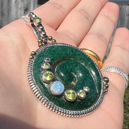 A men's aventurine koru necklace, accented with opal and peridot, shown at an angle in sunlight.