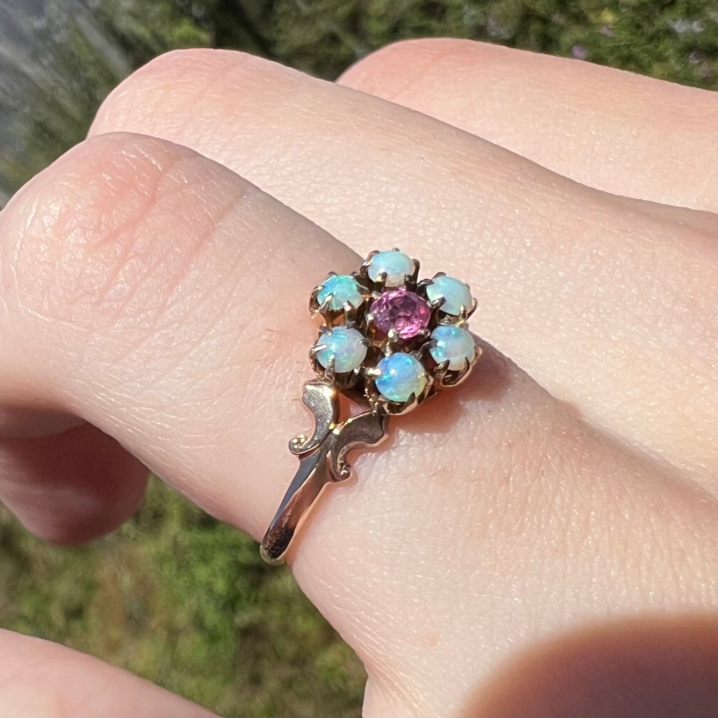Sunlit angled close-up of pink tourmaline and Hungarian opal ring in 9k gold, shown on finger
