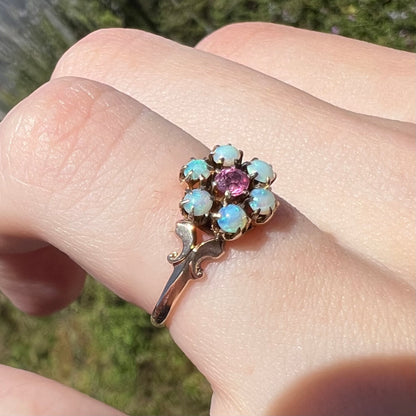 Sunlit angled close-up of pink tourmaline and Hungarian opal ring in 9k gold, shown on finger
