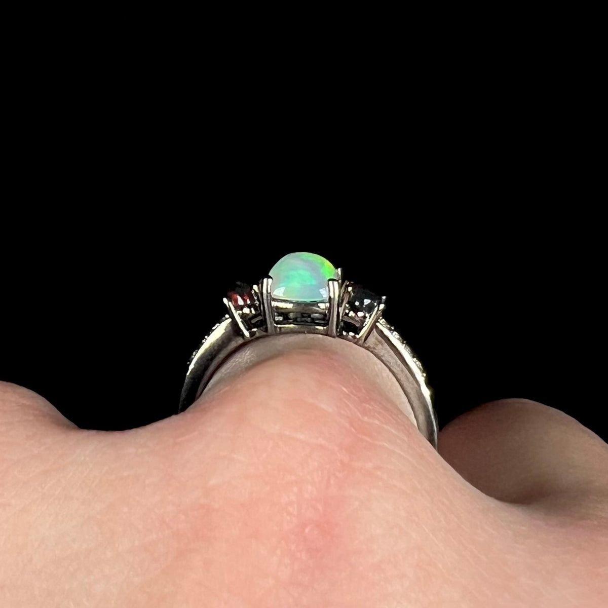 Side profile gallery view of three-stone opal ring with black rhodium plated finish, worn on finger