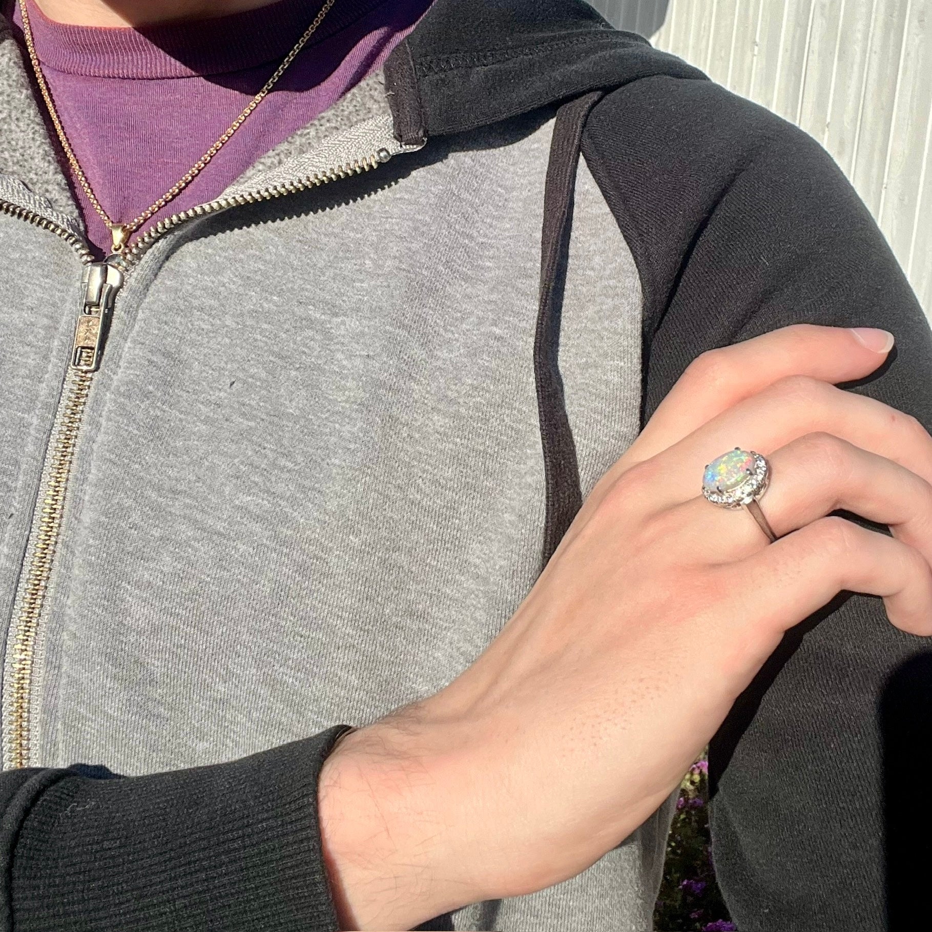 A vintage opal and diamond halo enggagement ring on a hand in the sunlight.