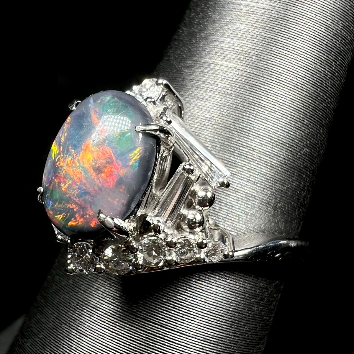 Side shoulder view of a dark opal ring set with geometric halo of diamond accents.  Round and tapered baguette cut diamonds in view.