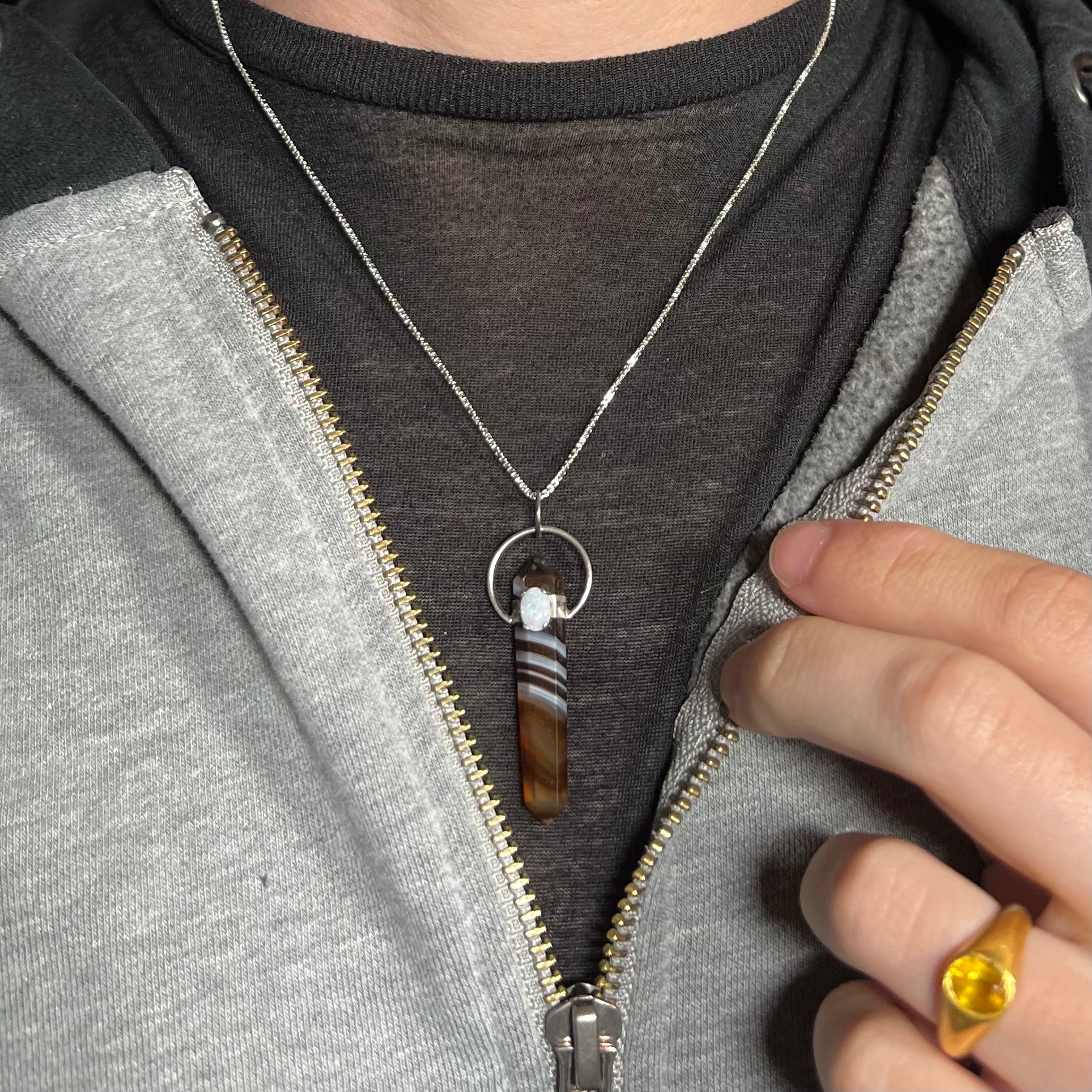 An opal and sardonyx crystal necklace, worn around a model's neck with a dark shirt and partially unzipped hoodie.