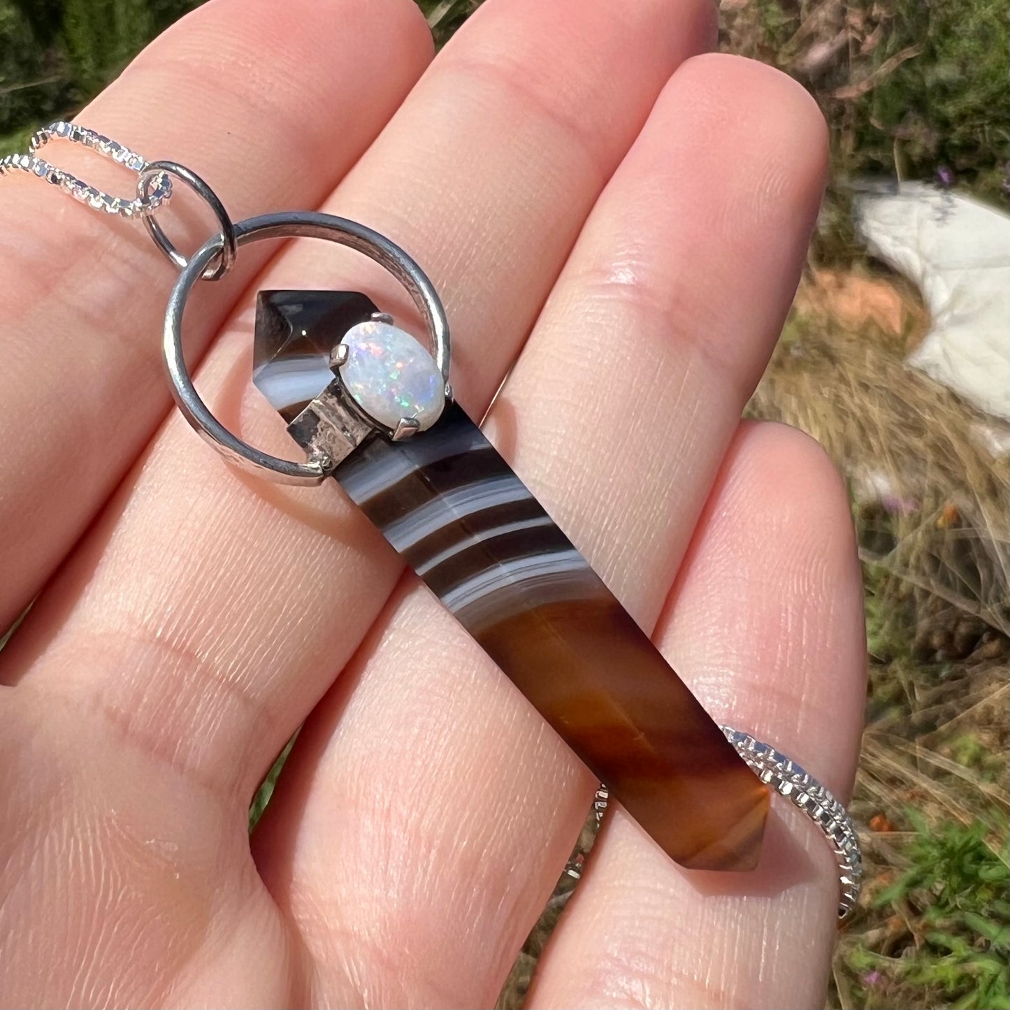An opal and sardonyx pendant held in the sunlight an an angle by a hand.