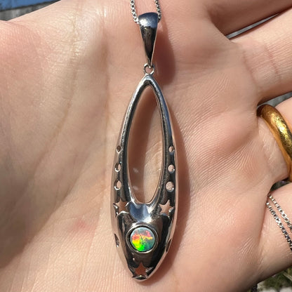 Close-up of a sterling silver and opal doublet ballerina shoe necklace in the sunlight.  The round opal is colorful.