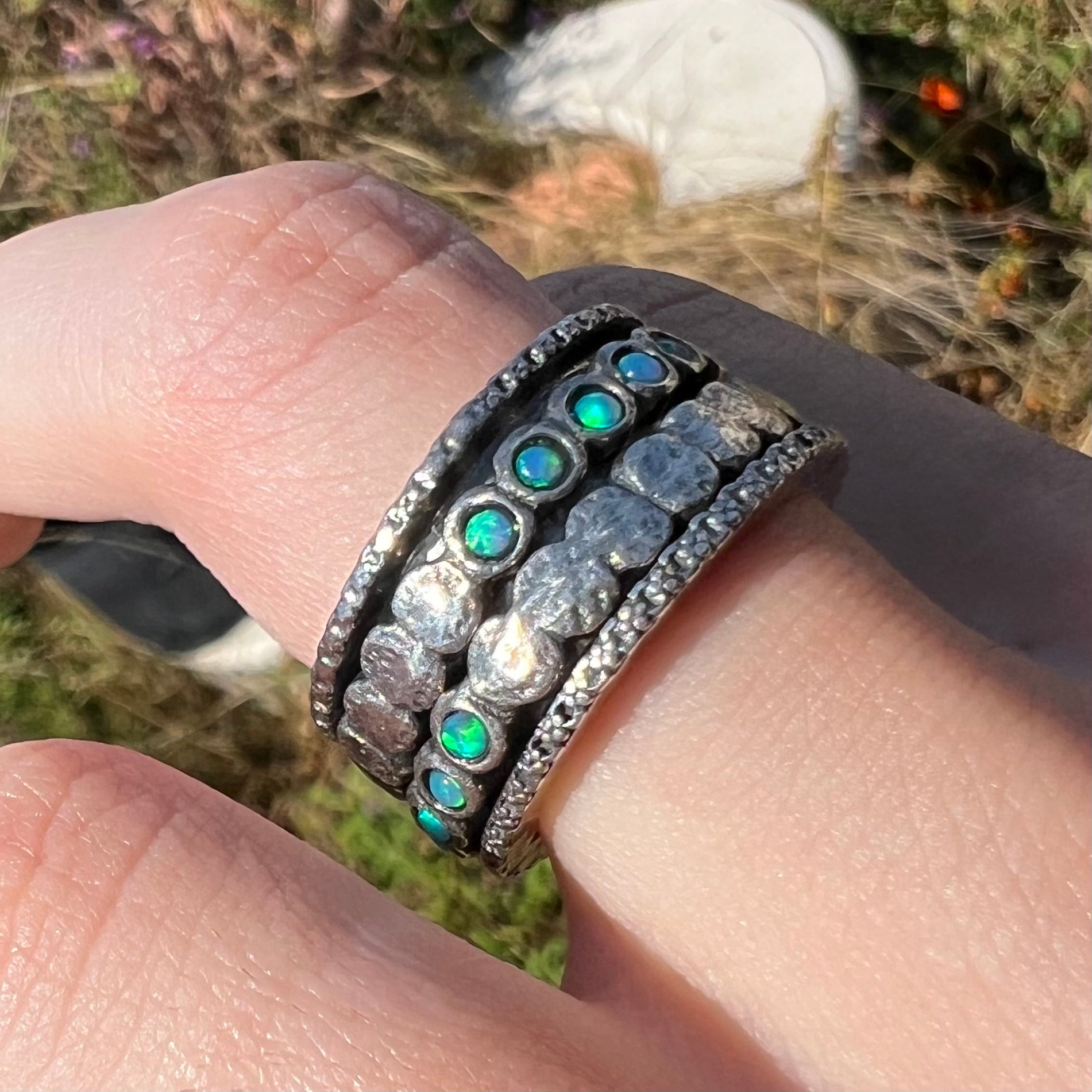 An opal spinner ring worn on a finger in sunlight.  The opals are round and show faint green color play.