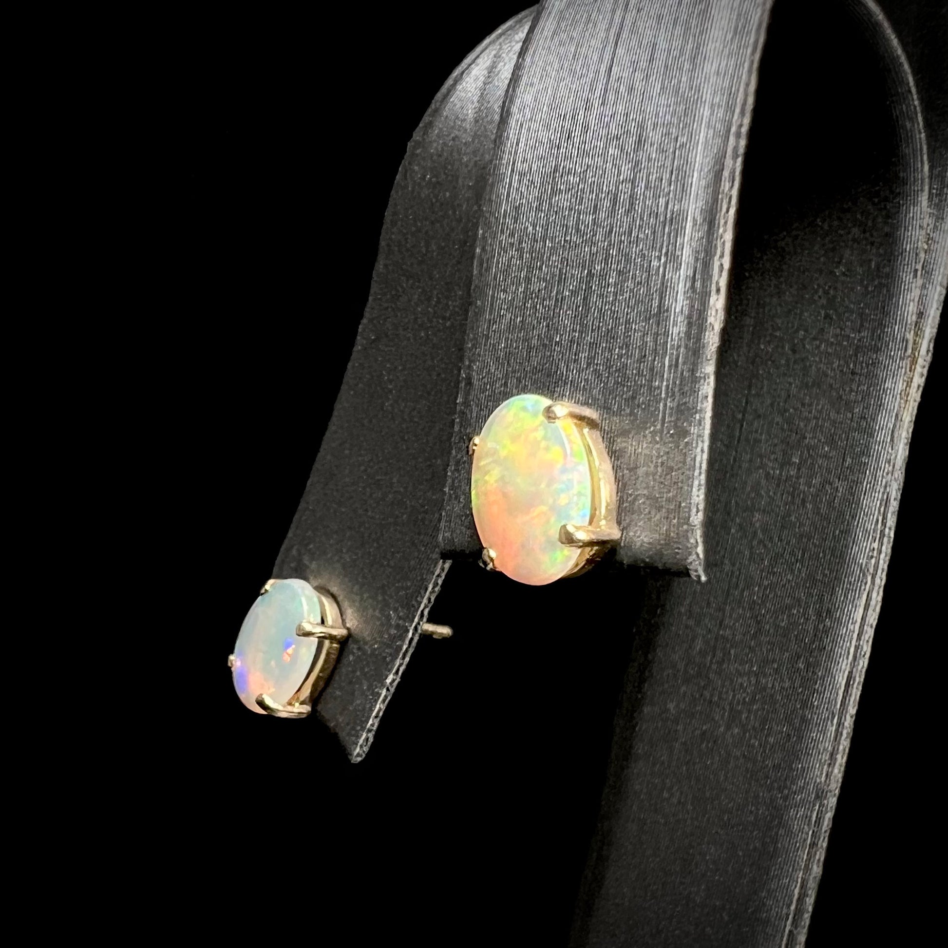 An angled view of 14k gold opal stud earrings, one opal showing yellow and red tones, the other subtle purple and pink.